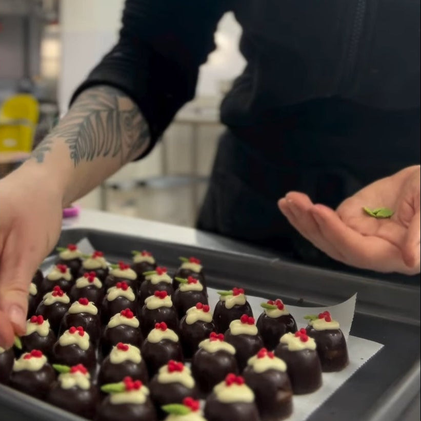 Person arranging small desserts on a tray in a kitchen setting